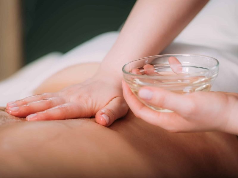 Massaging with massage oil, hands of a female massage therapist massaging a female client